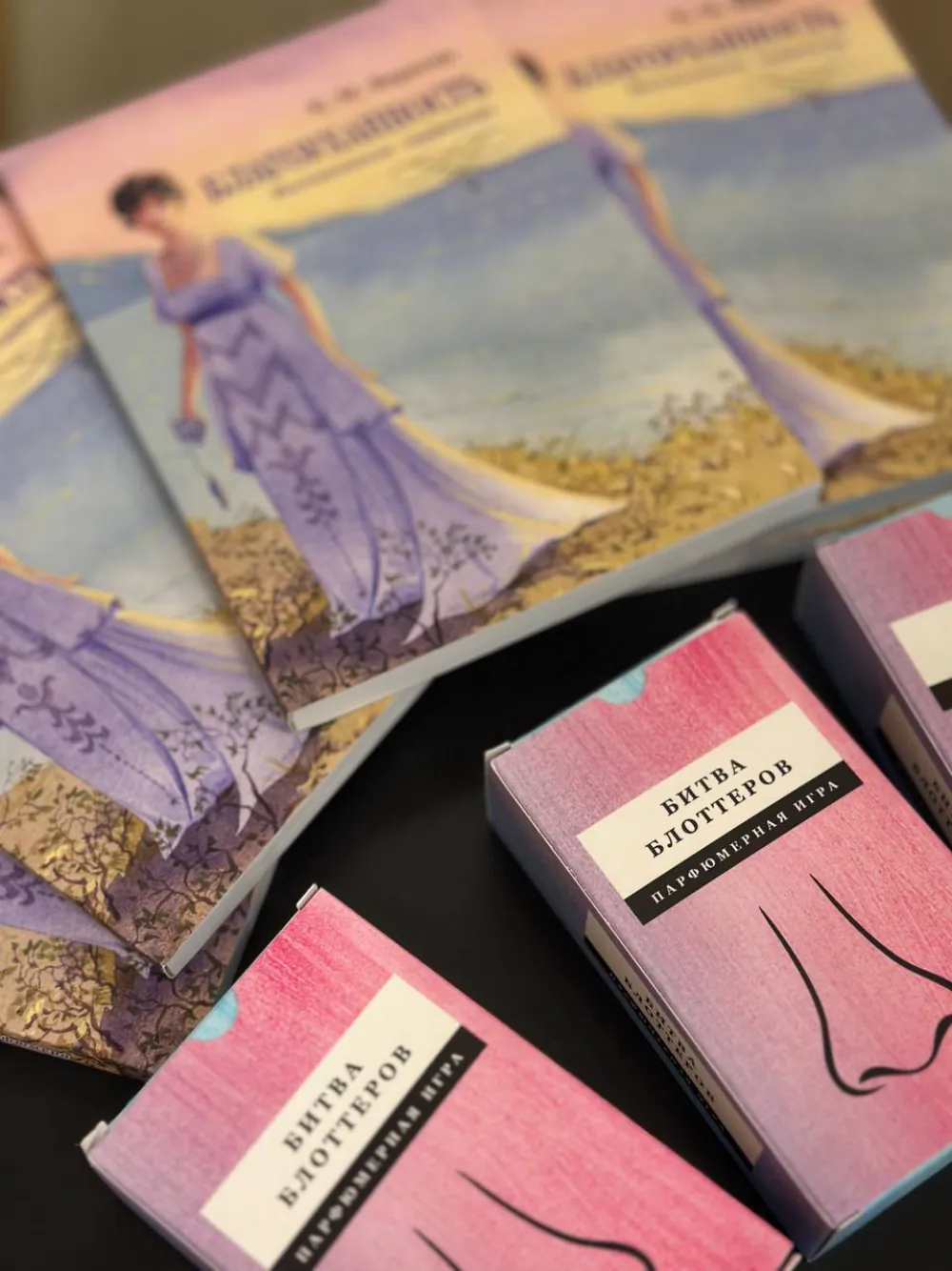 Коробки парфюмерной игры «Битва блоттеров» рядом с книгами